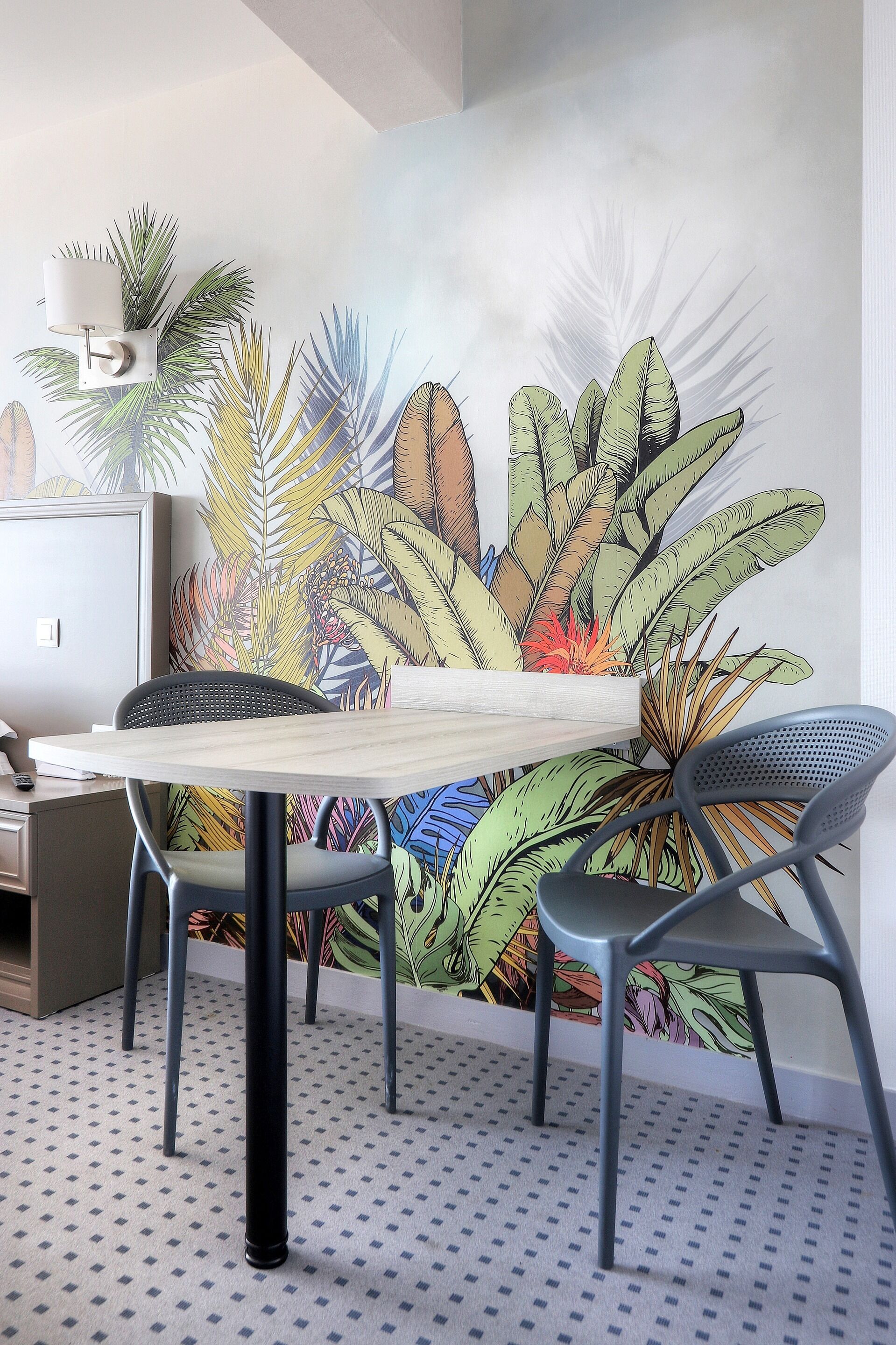 Een eetgedeelte met een tafel en stoelen, een wanddecoratie met tropische bladeren en een vloer met patroon.