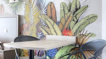 A dining area with a table and chairs, a wall mural with tropical leaves, and a patterned floor.