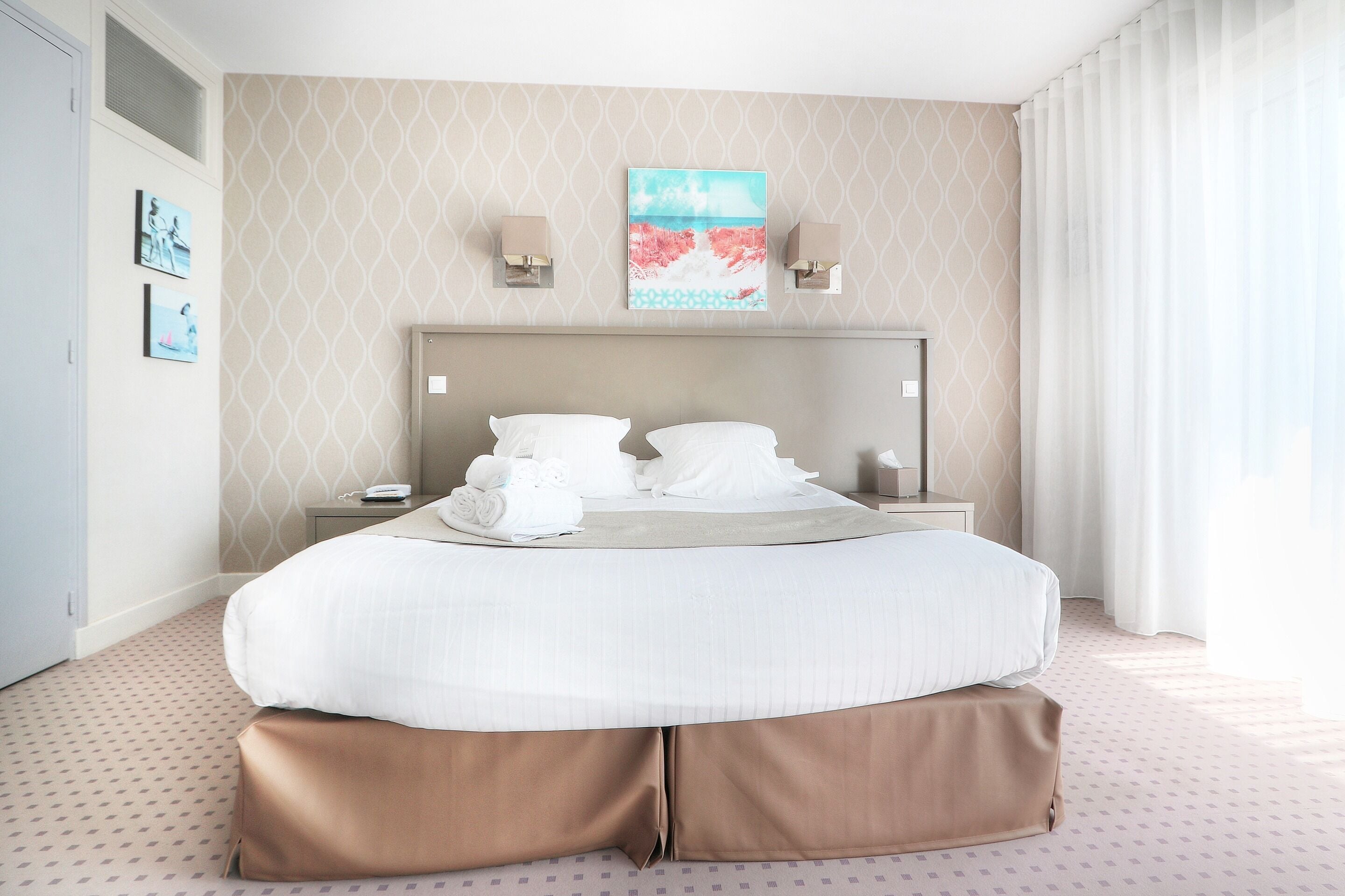 Una habitación de hotel con una cama grande, una mesita de noche, un cuadro en la pared y una ventana con cortinas.