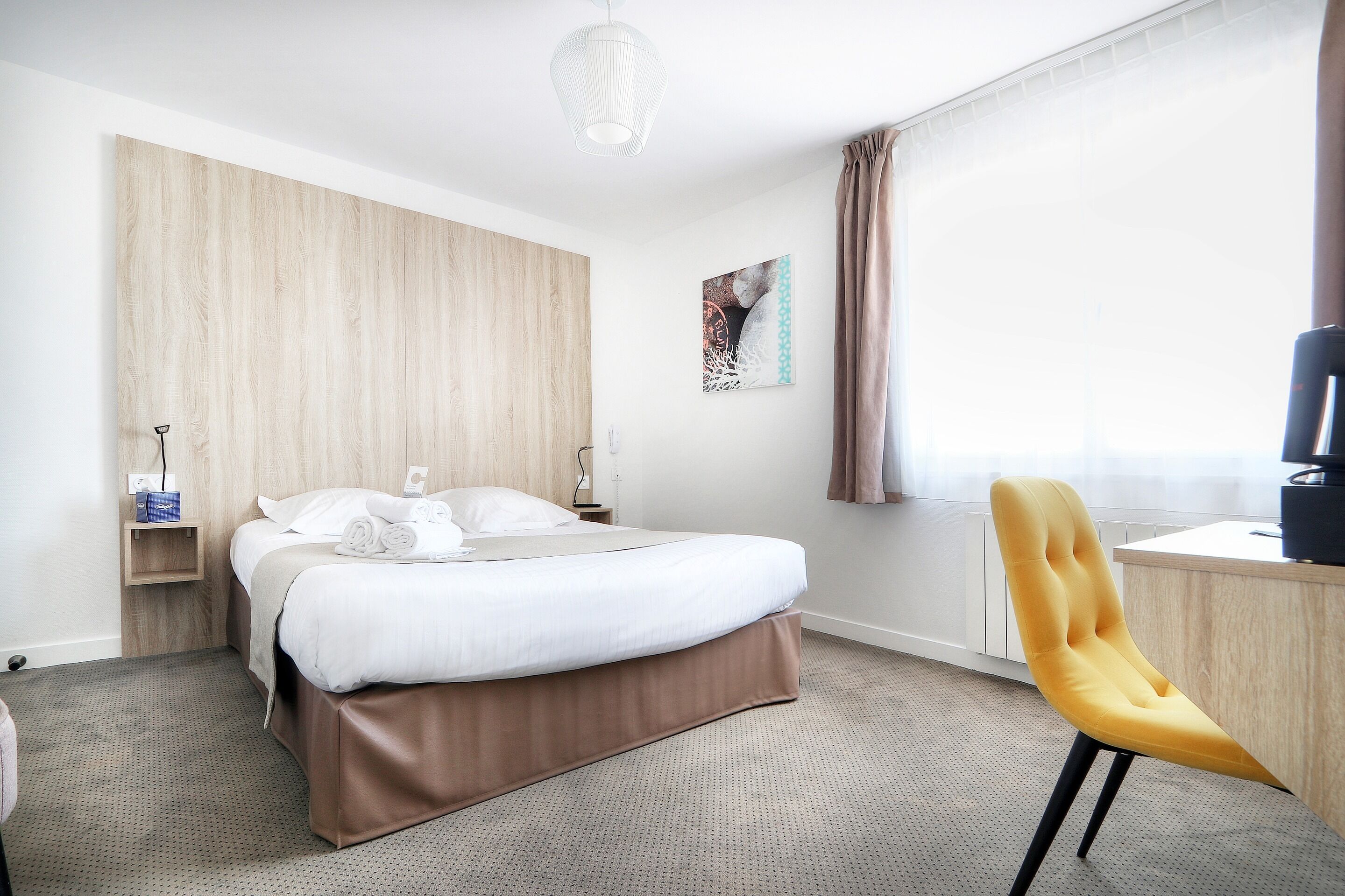 Una habitación de hotel con una cama, un escritorio, una silla, una mesita de noche y una obra de arte colgada en la pared.