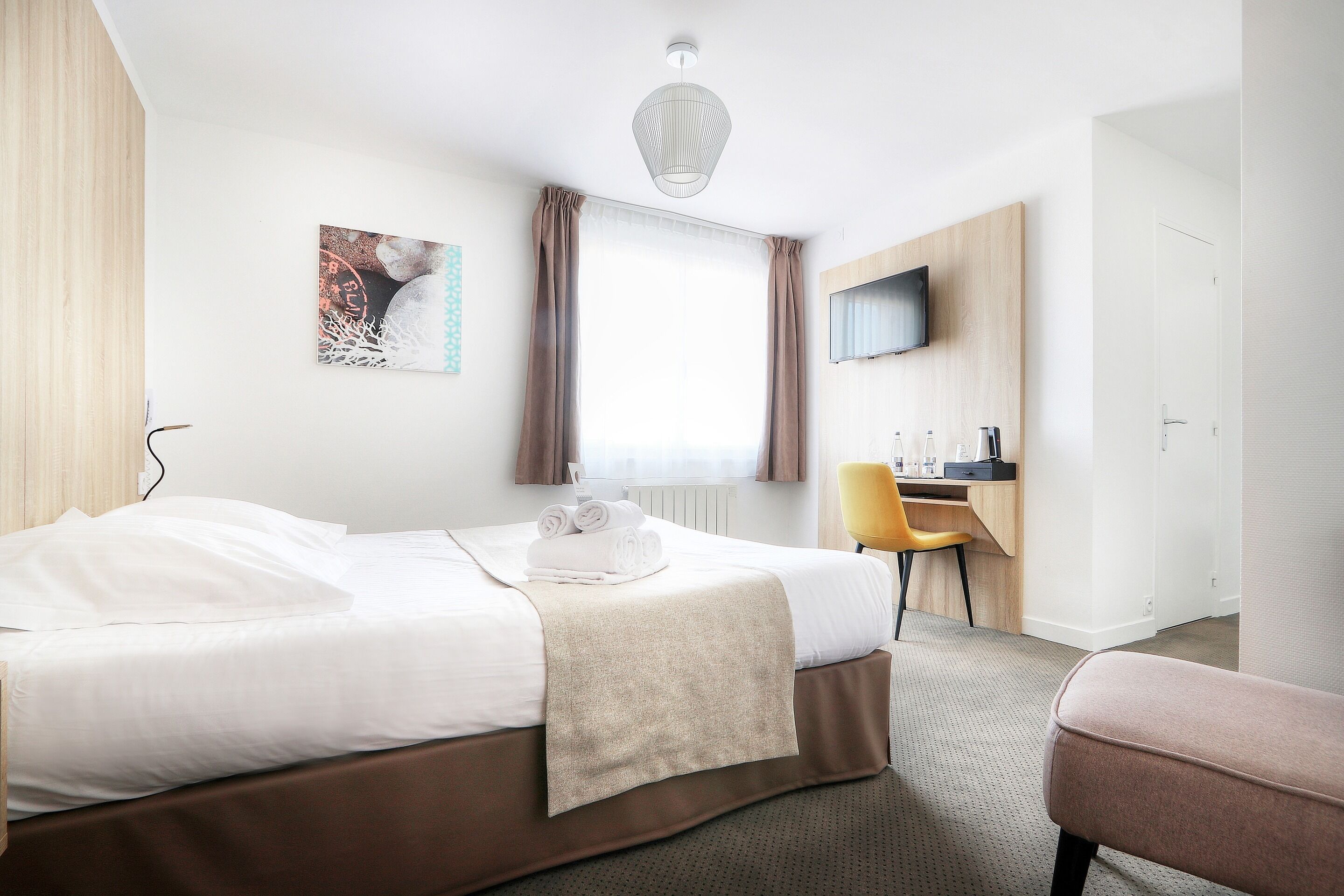 A hotel room with a bed, a desk, a chair, and a TV on the wall.