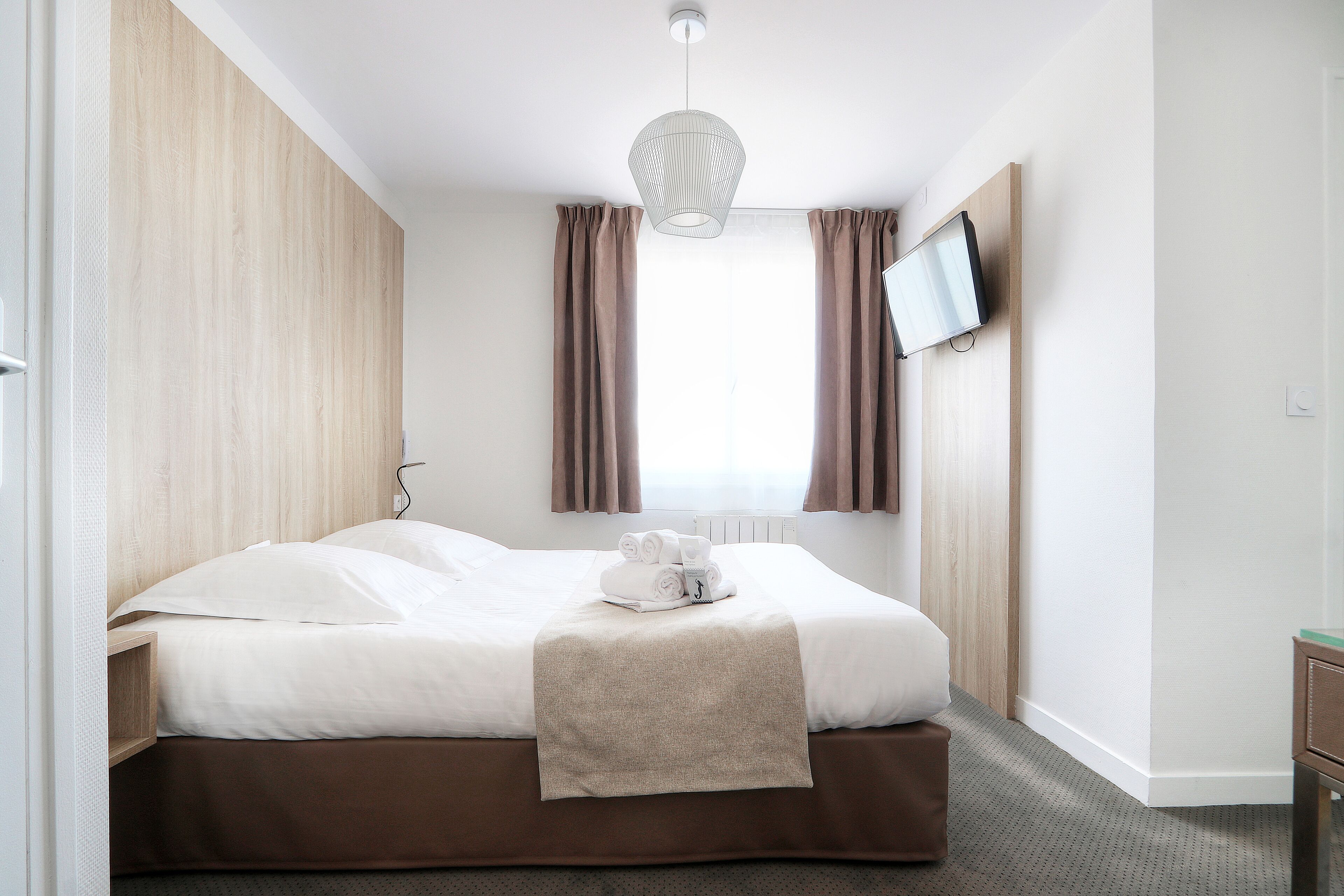 Habitación de hotel con cama, televisor en la pared y ventana con cortinas.