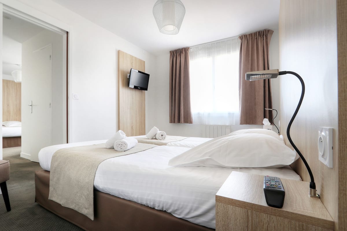 Ein Hotelzimmer mit Bett, Wand-Fernseher, Schreibtisch mit Lampe und einem Fenster mit Vorhängen.