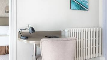 Een hotelkamer met een bed, een bureau met lamp, een aan de muur bevestigde televisie en een radiator.