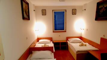 A hotel room with two beds, a small table, and a window with blinds.