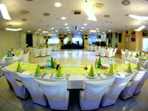 A banquet hall with round tables set for a formal event, featuring white tablecloths and green centerpieces.