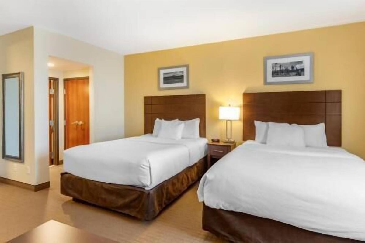 A hotel room with two beds, a wooden headboard, a nightstand with a lamp, and a framed picture on the wall.