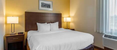 Ein Hotelzimmer mit einem großen Bett, zwei Nachttischen mit Lampen, einem Kopfteil, einem gerahmten Bild an der Wand und einem Fenster mit Vorhängen.