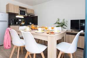 A modern kitchen with a dining table set for breakfast, including plates, cups, and a fruit bowl. - Maisonette in France with Modern Comfort (Noirmoutier en l'Ile)