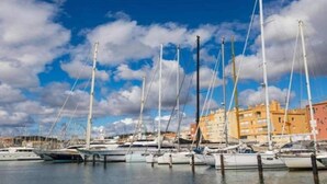 A marina with multiple sailboats docked, buildings in the background, and a partly cloudy sky. - Coastal Retreat w/ Balcony (LE CAP D'AGDE)