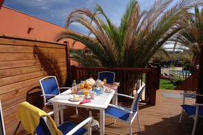 An outdoor patio with a table set for breakfast, surrounded by chairs, and a pool in the background. - Cap d’Agde Retreat w/ Terrace (LE CAP D'AGDE)