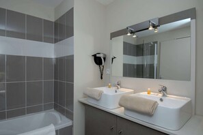 Een moderne badkamer met twee wastafels, een haardroger bevestigd aan de muur en een douchehoek.