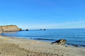 Ein Strand mit sandigem Ufer, ruhiger See und einer Klippe im Hintergrund.