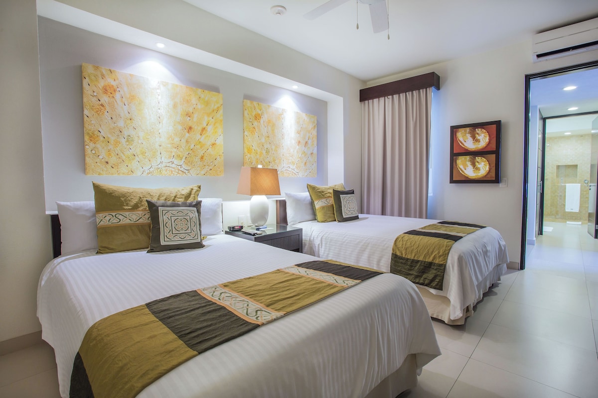 Una habitación de hotel con dos camas, un ventanal con cortinas y obras de arte en las paredes.