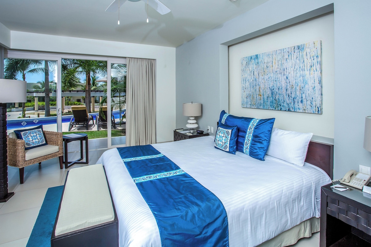 Habitación de hotel con una cama grande, vistas a una piscina, una silla y una mesa.