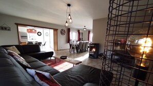 Een woonkamer met een bank, een eethoek met een tafel en stoelen, en een houtkachel.