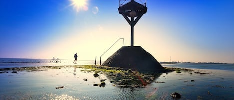 Ein Strand mit einem einzelnen Gebäude, einem Fahrrad und einer Person, die spazieren geht.