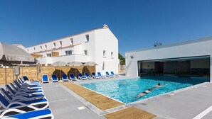 Ein Poolbereich mit Liegestühlen und Sonnenschirmen, ein Gebäude mit einem Ziegeldach und ein klarer, blauer Himmel.