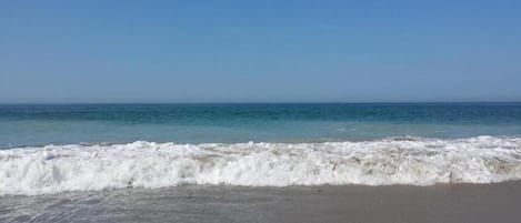 Une plage où les vagues se brisent près du rivage, sous un ciel dégagé.
