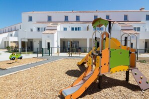 A playground with a slide and climbing structures, surrounded by a gravel area, with a building in the background. - Charming Stay by the Sea (Noirmoutier en l'Ile)