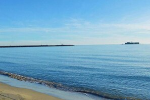 A calm sea with a sandy beach and a pier extending into the water.