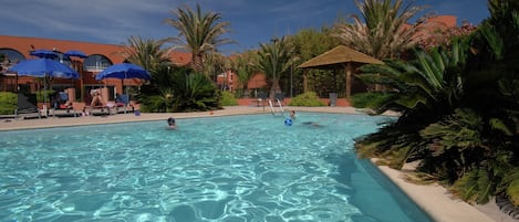 A swimming pool with clear water, surrounded by palm trees and lounge chairs.