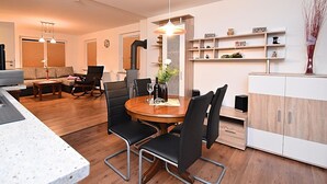 A modern living room with a dining area, featuring a wooden dining table, black chairs, a sofa, and a built-in cabinet. - Ferienhaus in Blankenburg (Blankenburg)
