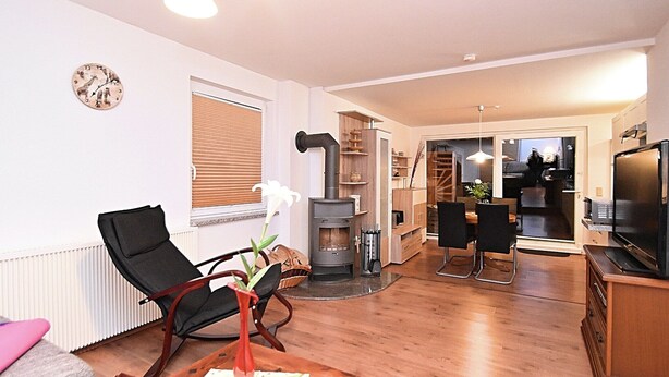 A modern living room with a fireplace, wooden furniture, and a dining area. - Ferienhaus in Blankenburg (Blankenburg)