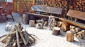 An outdoor seating area with wooden benches and chairs, a pile of firewood, and a cat. - Ferienhaus in Blankenburg (Blankenburg)