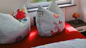 A bed with a red headboard and two decorative pillows with floral patterns. - Ferienhaus in Blankenburg (Blankenburg)