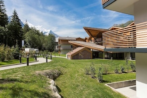 A modern building with a sloped roof, surrounded by a well-maintained lawn and a mountain backdrop. - Apartment in France with Heated Pool & Wellness (Chamonix mont blanc)