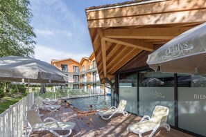 A poolside area with lounge chairs and umbrellas, a wooden deck, and a building with 'Odalys' branding.