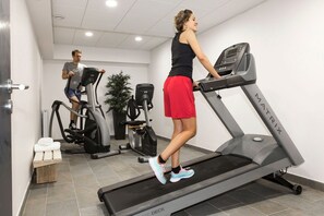 A gym with treadmills, a man and a woman exercising, and a small wooden bench. - Apartment in France with Heated Pool & Wellness (Chamonix mont blanc)