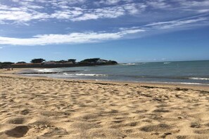 Ein sandiger Strand mit Wellen, einem klaren Himmel und einer entfernten, von Bäumen bewachsenen Insel.