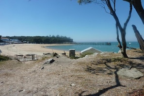 A beach with a wooden fence, a stone structure, and a pier extending into the water.