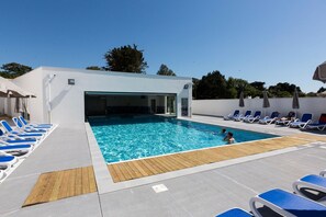 A swimming pool with clear blue water, surrounded by lounge chairs and umbrellas, and a covered area with a door leading to the pool.