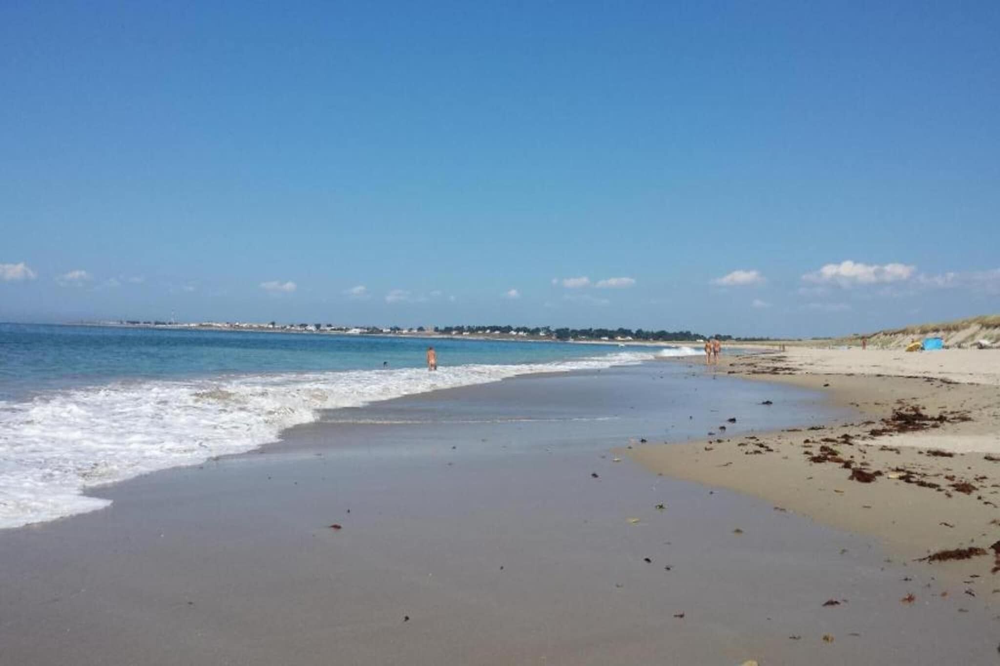A beach with a clear sky, calm sea, and a few people walking along the shore.