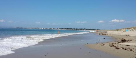 A beach with a clear sky, calm sea, and a few people walking along the shore.