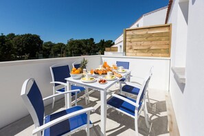 Une terrasse avec une table préparée pour le petit-déjeuner, comprenant des fruits, du pain et des boissons.