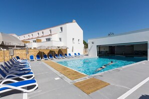 Ein Poolbereich mit Liegestühlen und Sonnenschirmen, ein Gebäude mit einem Ziegeldach und ein klarer, blauer Himmel.