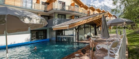 Ein Poolbereich mit Holzterrasse, Liegestühlen und Sonnenschirmen.
