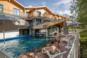 Ein Poolbereich mit Holzterrasse, Liegestühlen und Sonnenschirmen.