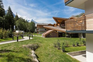 Ein modernes Gebäude mit geneigtem Dach, umgeben von einer gepflegten Rasenfläche und einem Bergpanorama.