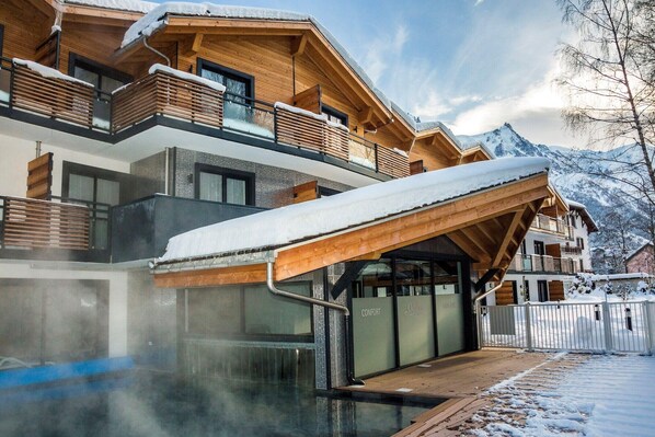 A multi-story wooden building with a covered outdoor area and a view of snow-covered mountains.