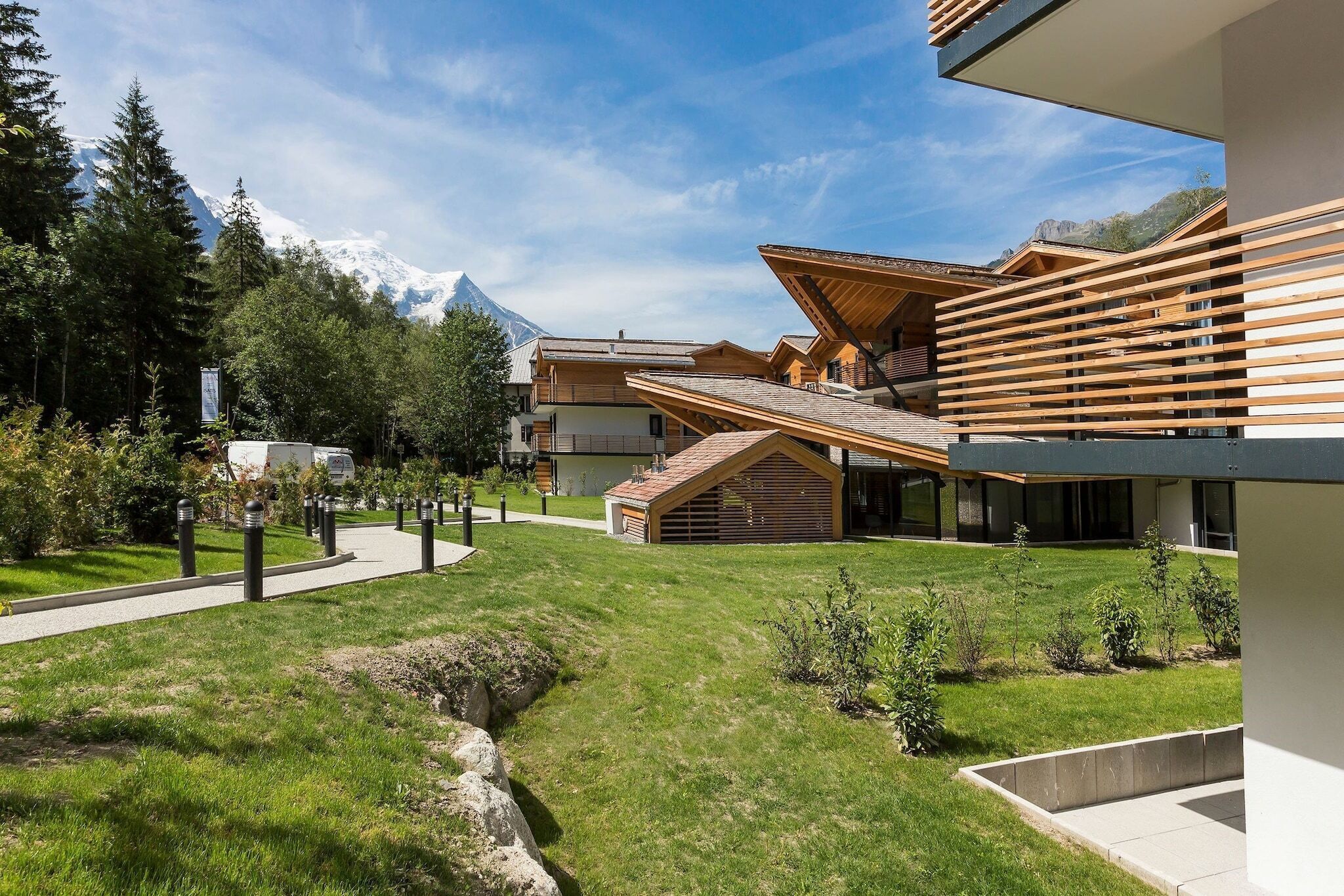 A modern building with a sloped roof, surrounded by a well-maintained lawn and a mountain backdrop.