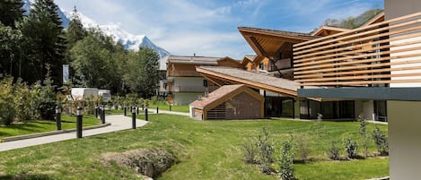A modern building with a sloped roof, surrounded by a well-maintained lawn and a mountain backdrop.