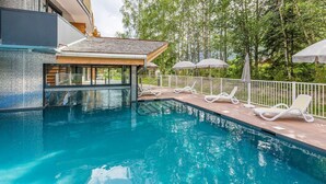 A swimming pool with lounge chairs and umbrellas, surrounded by a wooden deck and a white fence. - Alpine Comfort near Slopes (chamonix mont blanc)