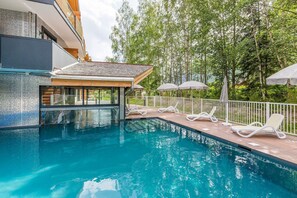 A swimming pool with lounge chairs and umbrellas, surrounded by a wooden deck and a white fence. - Alpine Comfort near Slopes (chamonix mont blanc)