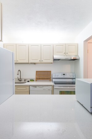 A kitchen with white cabinets, a stainless steel range hood, a dishwasher, and a stove. - Harvard Square Apartments by Next Star (Cambridge)