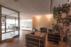 A waiting area with leather chairs, a reception desk, and a large window offering a view of the outside. - Harvard Square Apartments by Next Star (Cambridge)